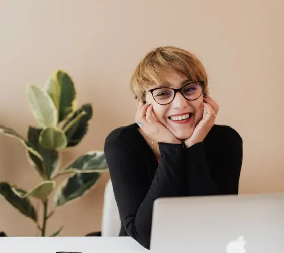 Cheerful woman smiling while sitting at table with laptop